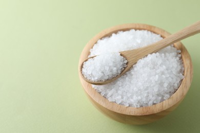 Photo of Organic white salt in bowl and spoon on olive background, closeup. Space for text