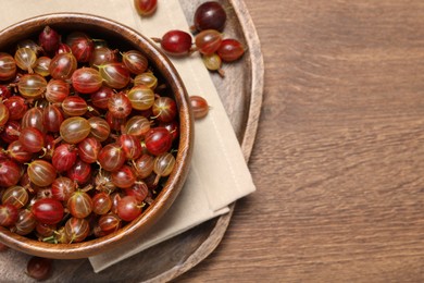 Bowl of fresh ripe gooseberries on wooden table, top view. Space for text