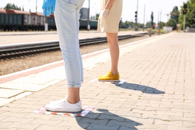 Photo of People standing on taped floor markings for social distance at train station, closeup. Coronavirus pandemic