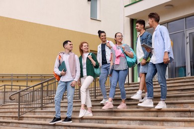 Photo of Group of happy young students walking down stairs outdoors
