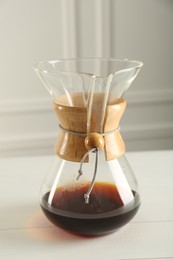 Photo of Glass chemex coffeemaker with coffee on white table, closeup