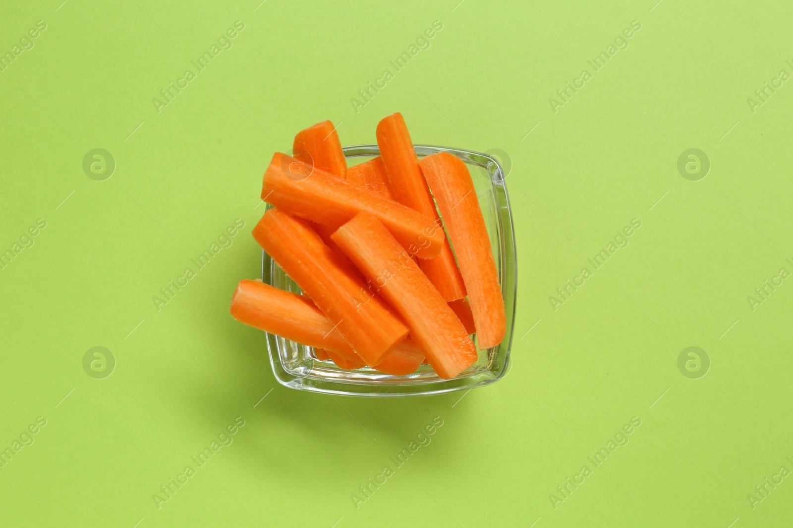 Photo of Cut fresh carrot in bowl on green background, top view. Finger food