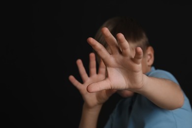 Photo of Boy making stop gesture against black background, focus on hands and space for text. Children's bullying