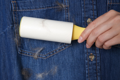 Woman removing hair from denim shirt with lint roller, closeup