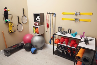 Many different sports equipment in room with beige walls