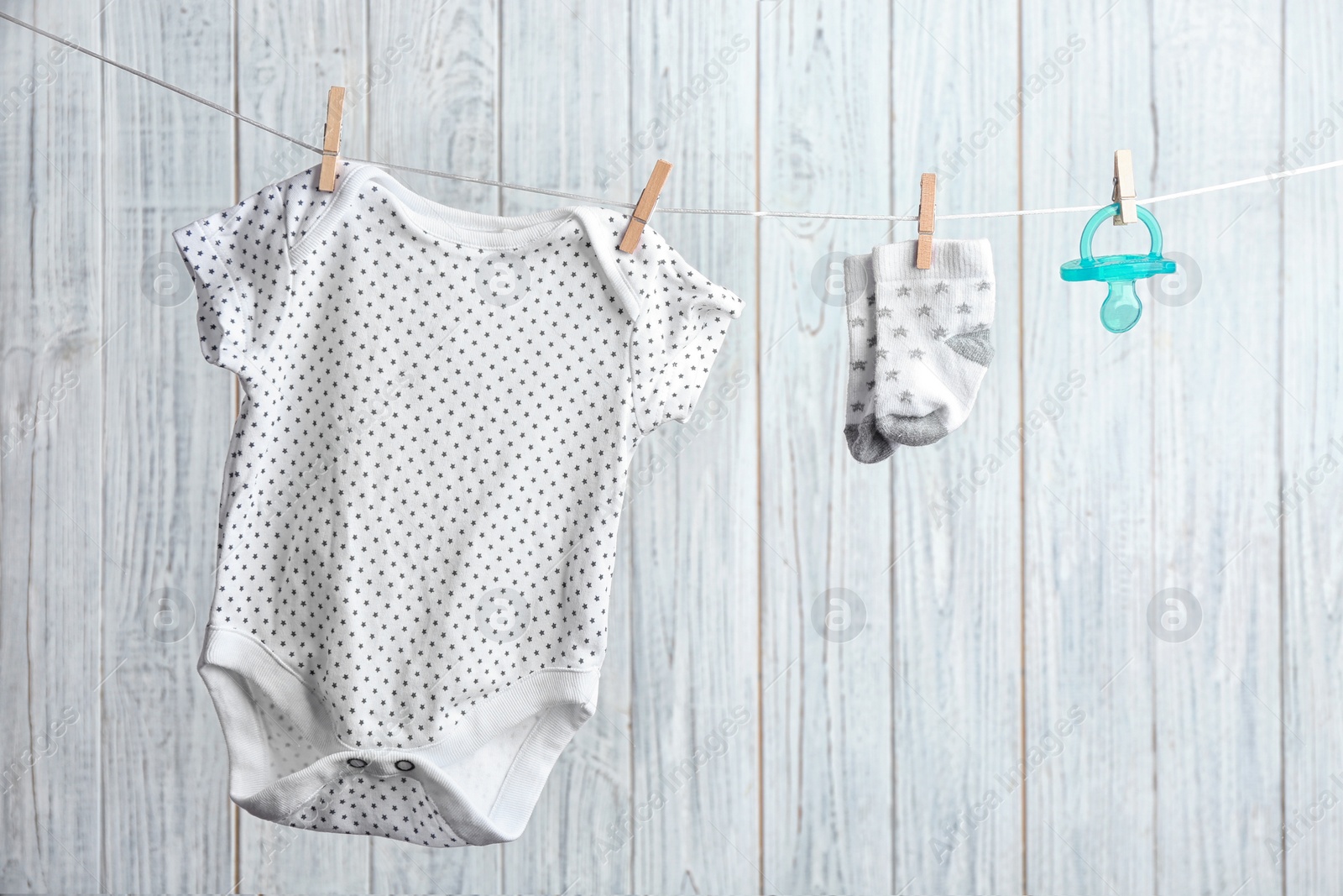 Photo of Bodysuit, pair of socks and pacifier on laundry line against wooden background. Baby accessories