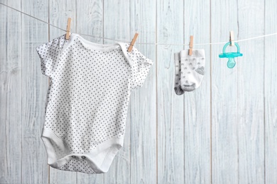 Photo of Bodysuit, pair of socks and pacifier on laundry line against wooden background. Baby accessories