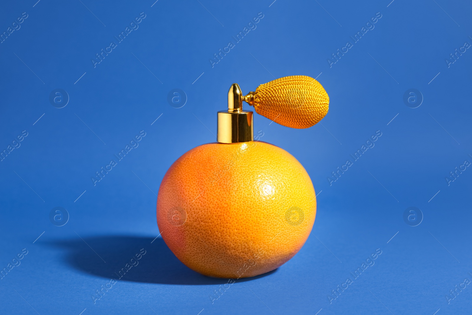 Photo of Grapefruit with vintage atomizer imitating perfume on blue background