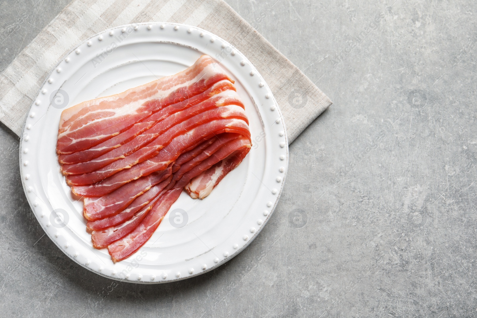 Photo of Plate with raw bacon rashers on grey background