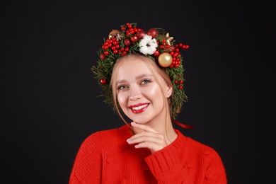 Beautiful young woman wearing Christmas wreath on black background