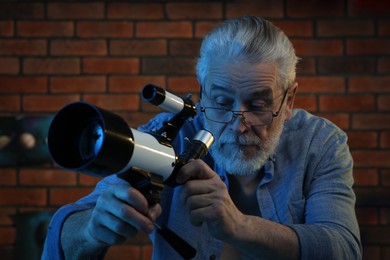 Senior man looking at stars through telescope in room