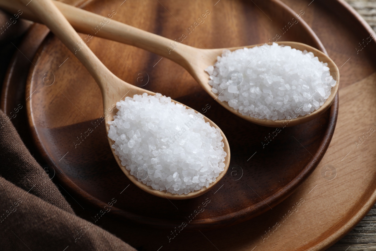 Photo of Organic salt in spoons on wooden table, closeup