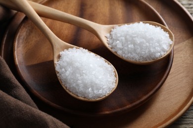 Photo of Organic salt in spoons on wooden table, closeup