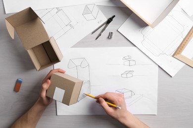 Photo of Man creating packaging design at light wooden table, top view