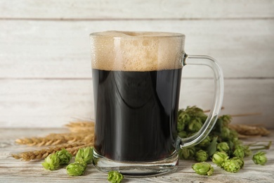 Composition with tasty beer, wheat spikes and fresh green hops on wooden table