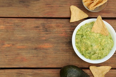 Photo of Delicious guacamole, avocado and nachos on wooden table, flat lay. Space for text