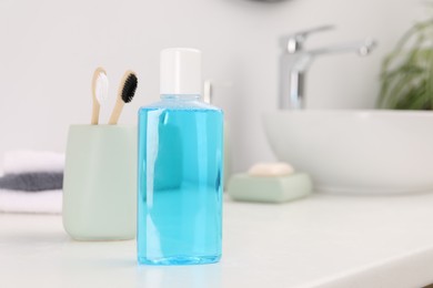 Bottle of mouthwash and toothbrushes on white table in bathroom, space for text