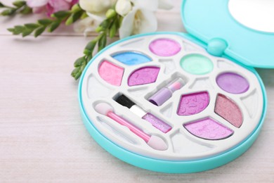Photo of Decorative cosmetics for kids. Eye shadow palette and flowers on white wooden table, closeup. Space for text