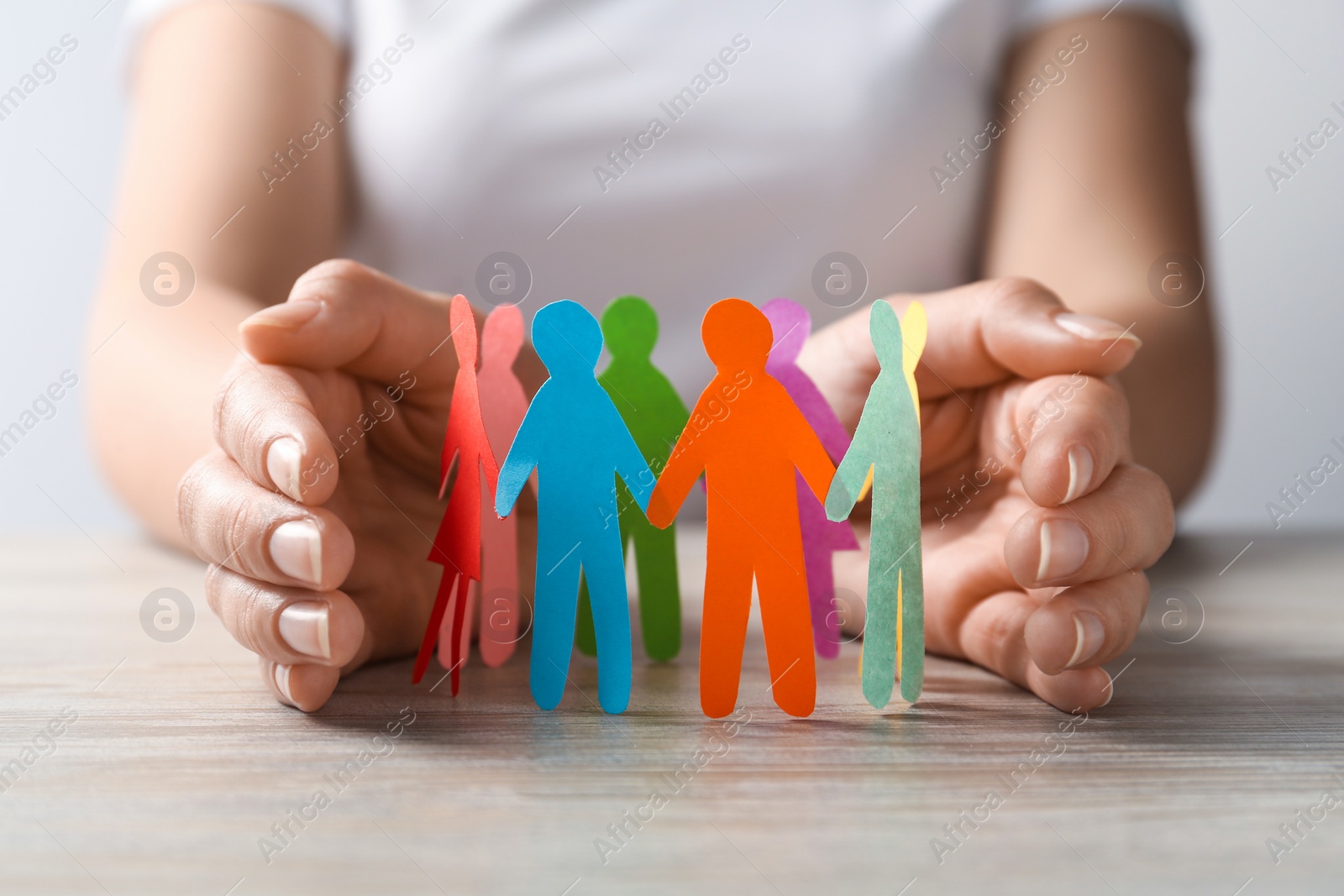 Photo of Woman protecting paper human figures on wooden table, closeup. Diversity and inclusion concept