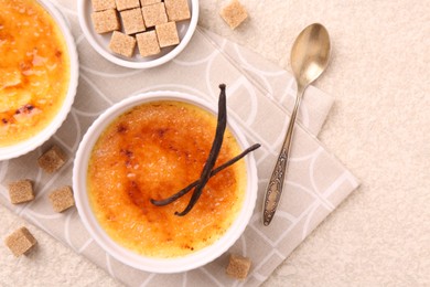 Photo of Delicious creme brulee in bowls, vanilla pods, sugar cubes and spoon on light textured table, top view