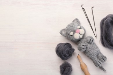 Photo of Felted cat, wool, needles and holder on light wooden table, flat lay. Space for text