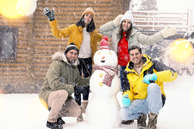 Happy friends near snowman outdoors on snowy day. Winter vacation