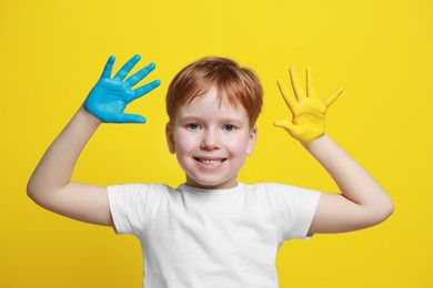Photo of Little boy with hands painted in Ukrainian flag colors on yellow background. Love Ukraine concept