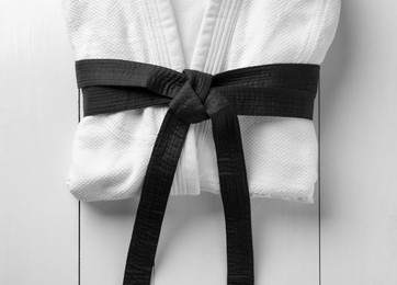 Photo of Martial arts uniform with black belt on white wooden background, top view