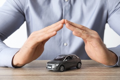 Photo of Male insurance agent covering toy car at table, closeup