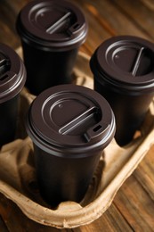 Takeaway paper coffee cups in cardboard holder on wooden table, closeup