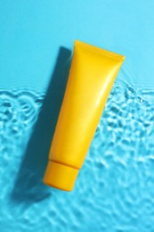 Tube with moisturizing cream in water on light blue background, top view