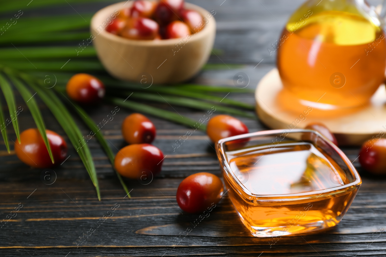 Photo of Palm oil in glass bowl, tropical leaf and fruits on wooden table. Space for text