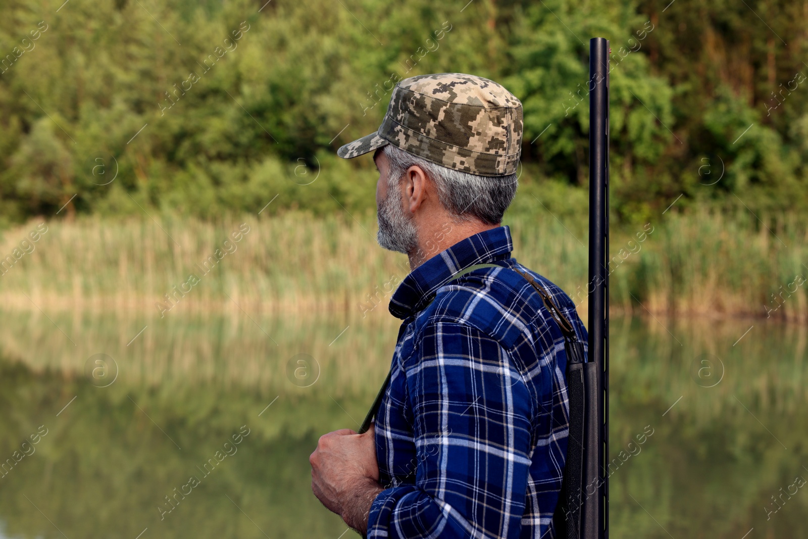 Photo of Man with hunting rifle near lake outdoors. Space for text