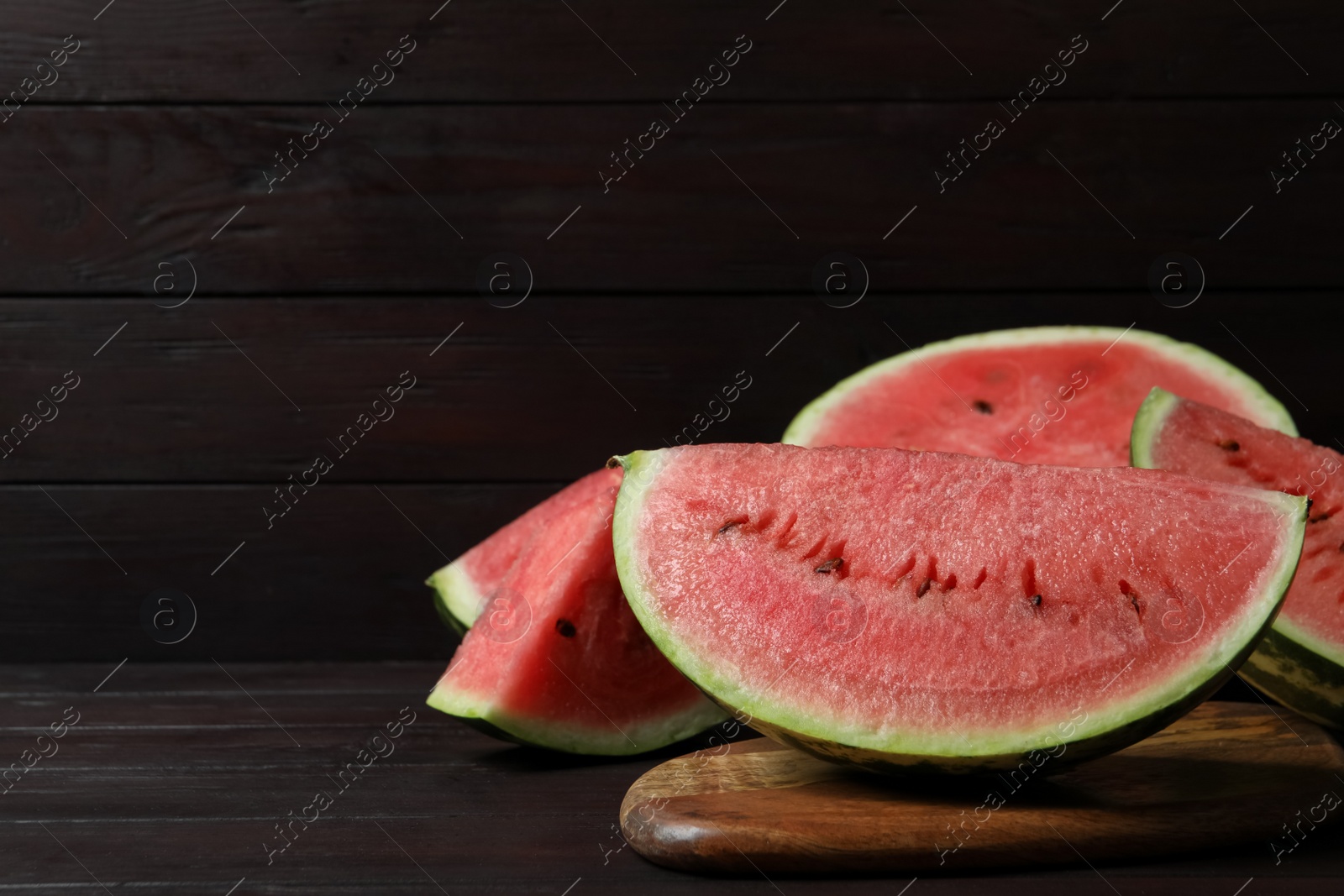 Photo of Slices of tasty ripe watermelon on dark wooden table, space for text