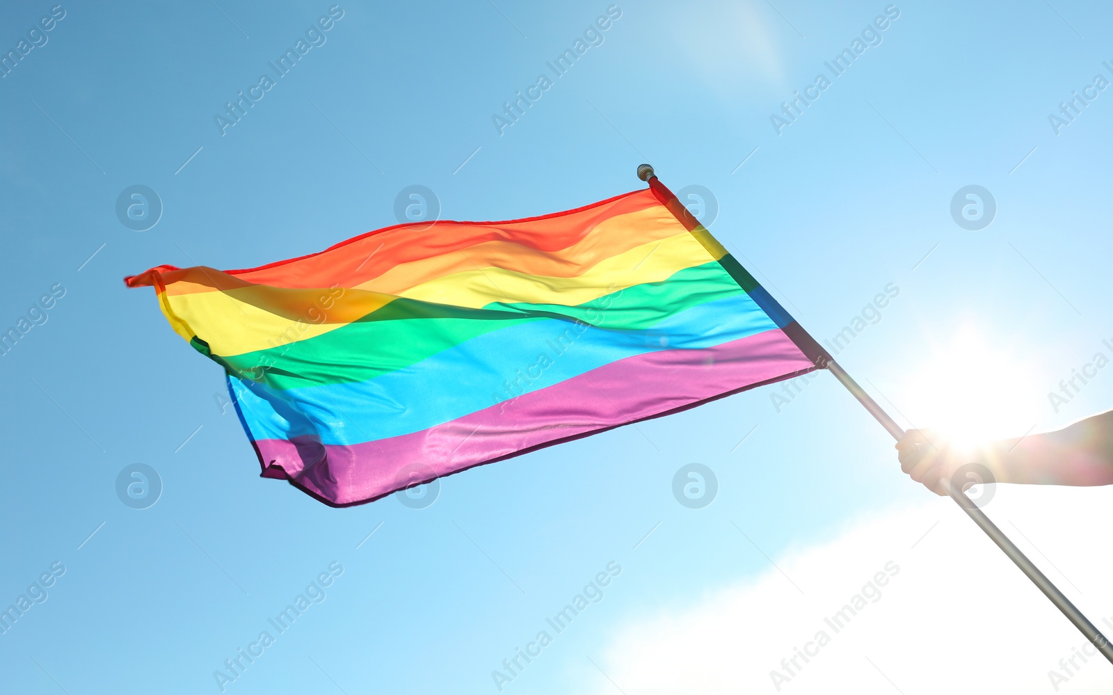 Photo of Gay man holding rainbow LGBT flag against blue sky