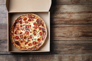 Delicious quiche with prosciutto and tomatoes in delivery box on wooden table, top view. Space for text