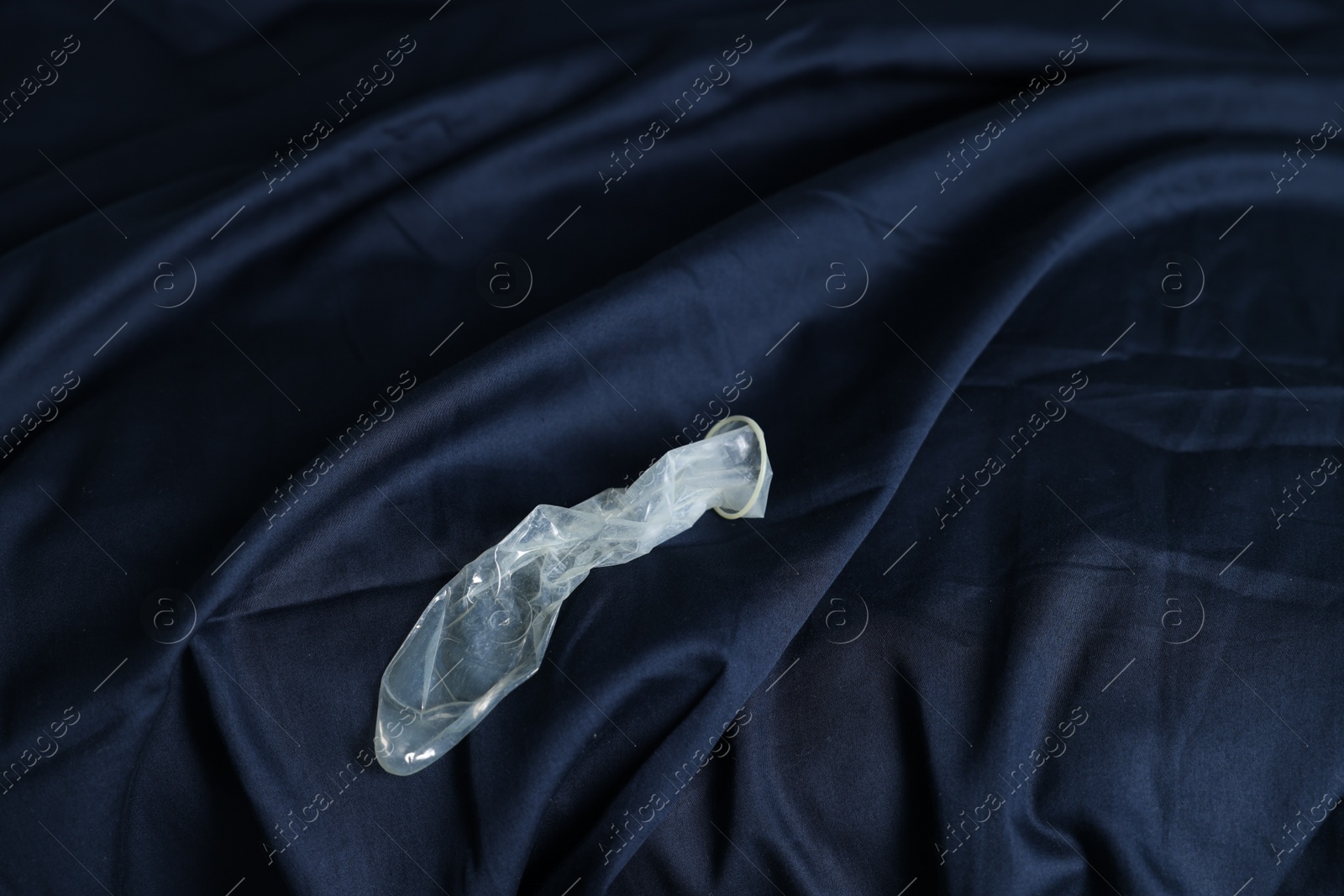 Photo of Unrolled condom on bed, above view. Safe sex