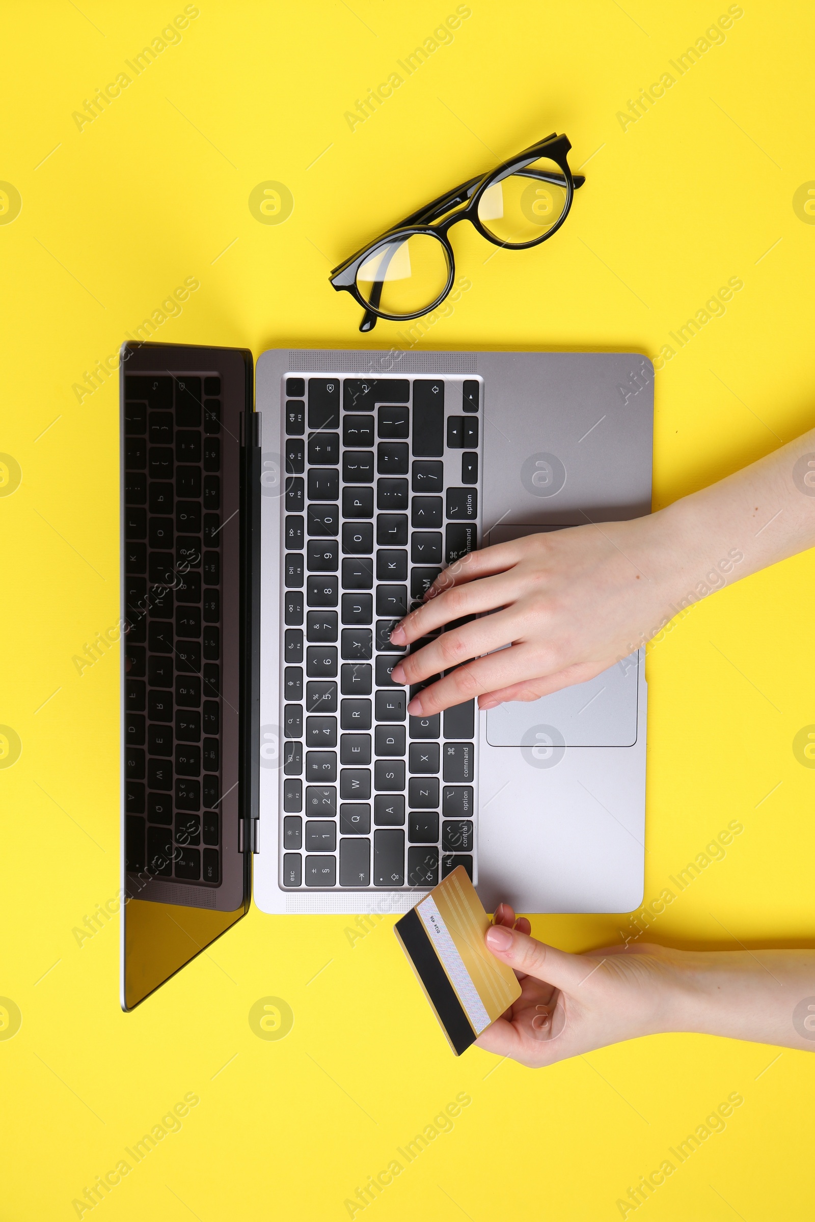 Photo of Online payment. Woman with laptop, credit card and glasses on yellow background, top view