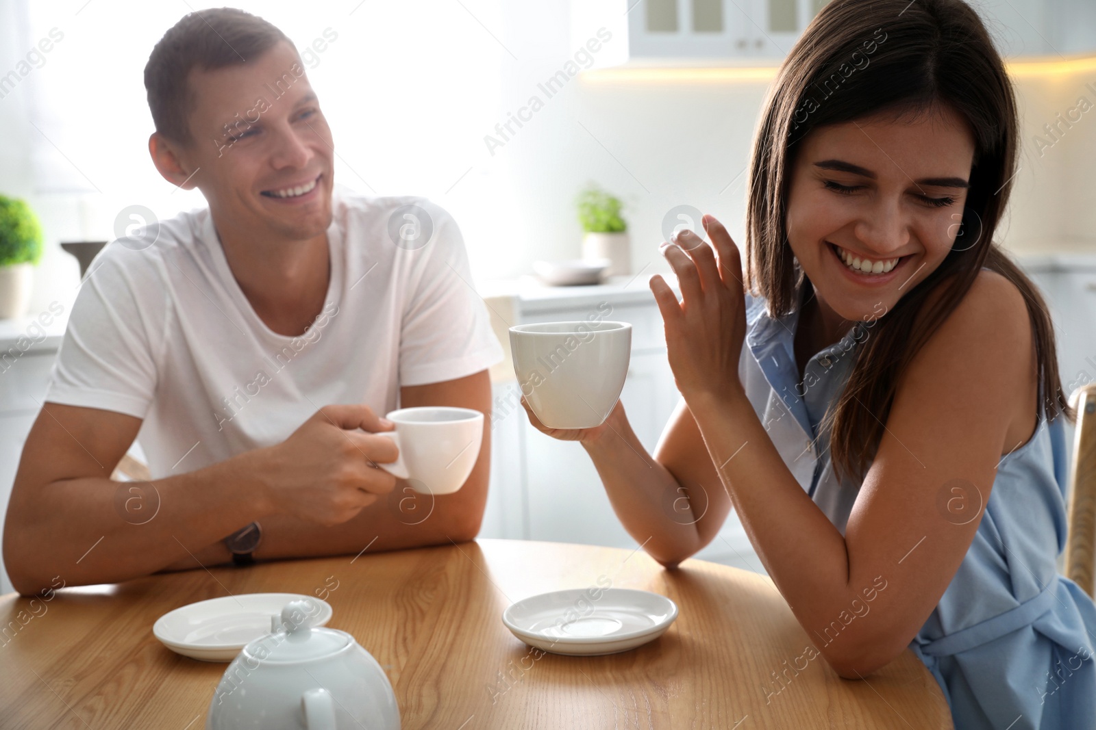 Photo of Man and woman talking while drinking tea at table in kitchen