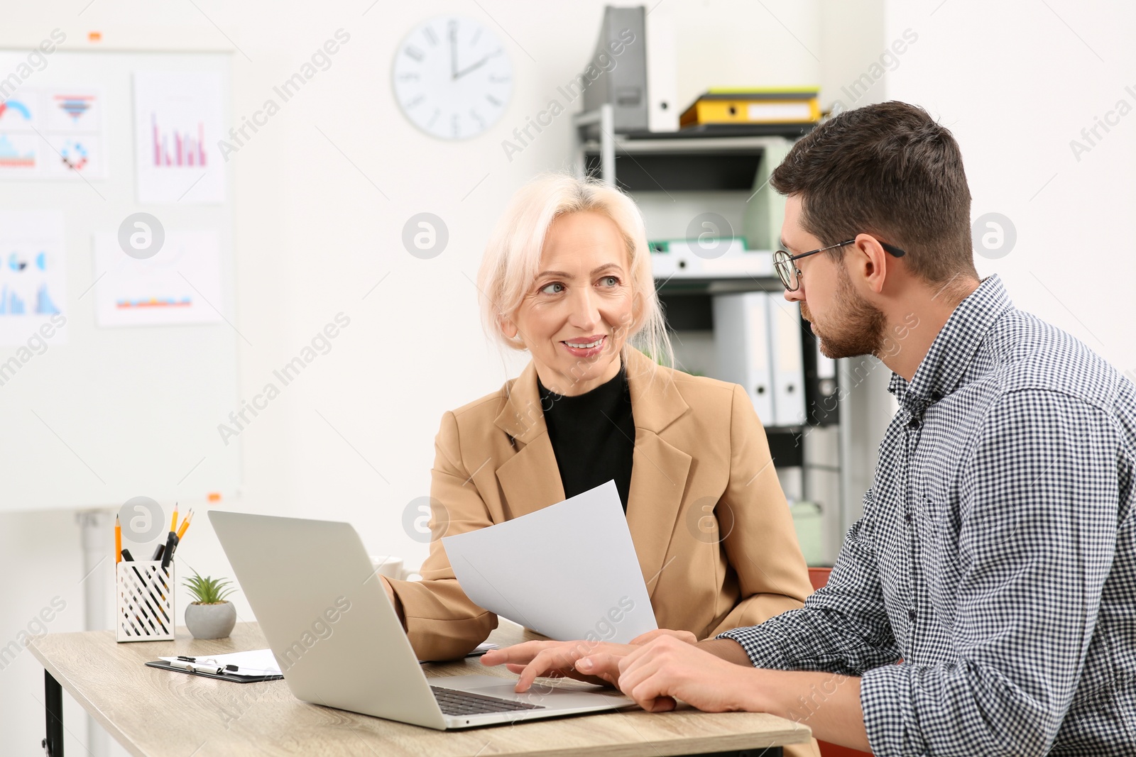 Photo of Boss and employee with laptop discussing work issues at wooden table in office