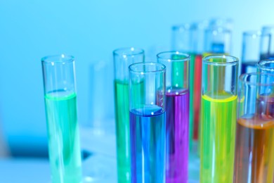 Photo of Many test tubes with colorful liquids on blurred background, closeup