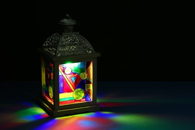 Photo of Decorative Arabic lantern on table against dark background. Space for text