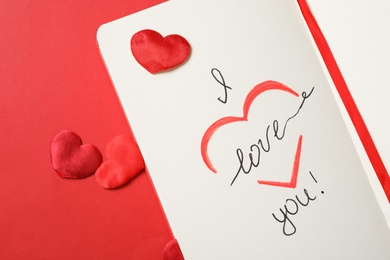 Photo of Notebook with text I Love You and hearts on red background, flat lay