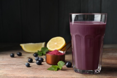 Photo of Tasty acai drink in glass, berries and powder on wooden table