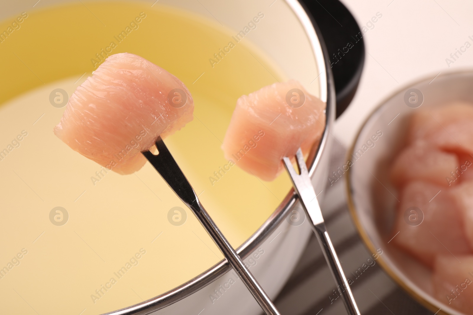 Photo of Fondue pot with oil, forks and raw meat pieces on white table, closeup