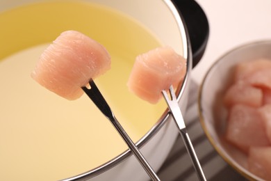 Fondue pot with oil, forks and raw meat pieces on white table, closeup