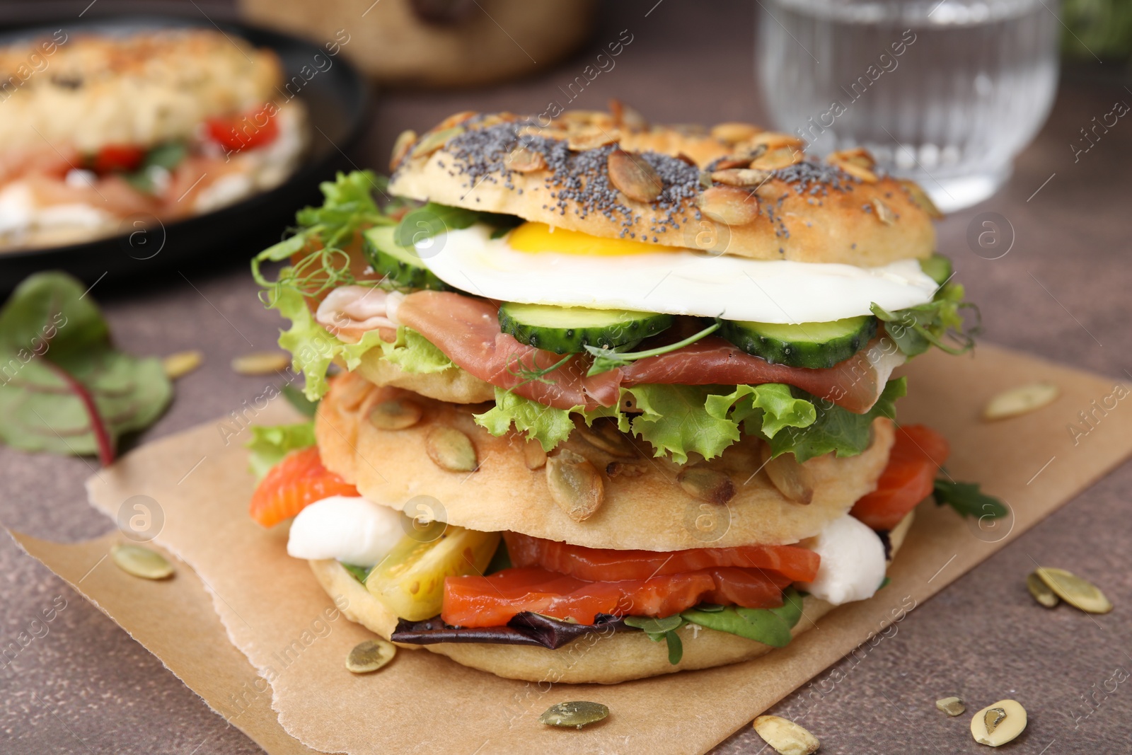 Photo of Tasty bagel with cured ham, egg, salmon and vegetables on brown table, closeup