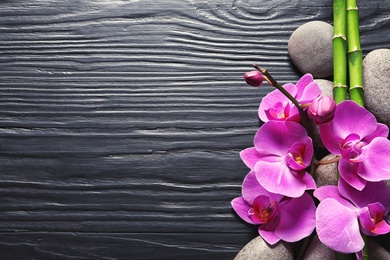 Photo of Spa stones with orchid flowers and bamboo on dark wooden background, top view. Space for text