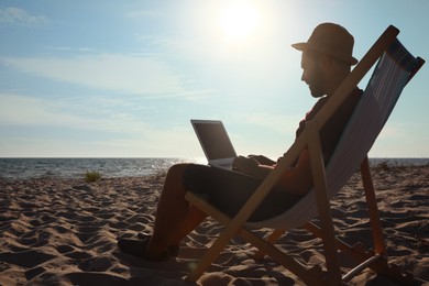 Photo of Man working with laptop in deck chair on beach