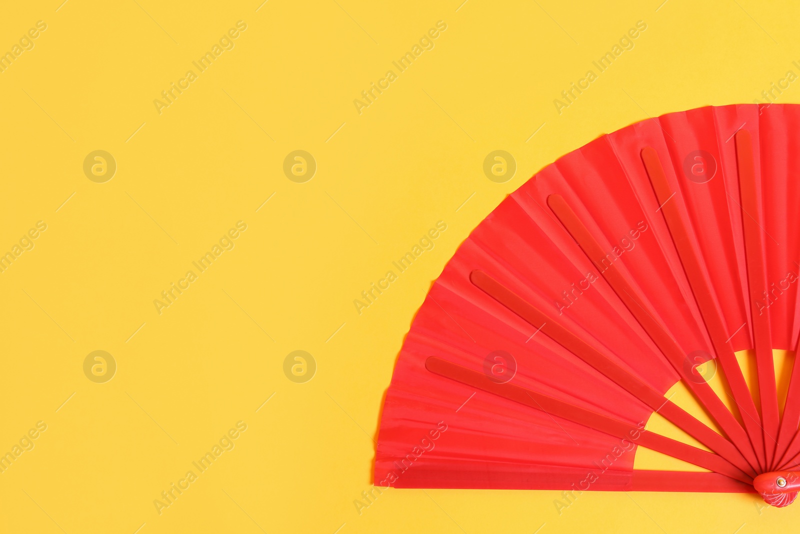 Photo of Red hand fan on yellow background, top view. Space for text